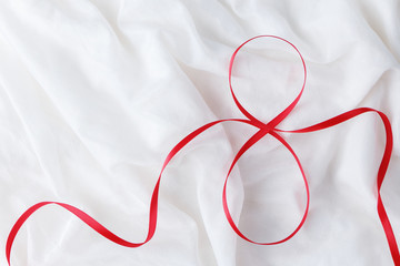 Red ribbon in shape of number eight on white fabric background