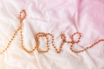 Beads in the shape of a word Love on a white fabric background