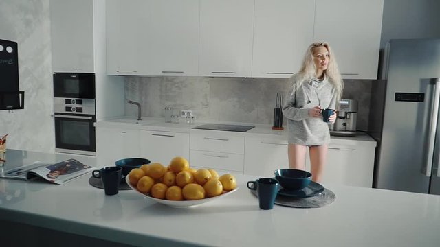 Woman cooks coffee on coffee maker and sits at the table. She quietly reads her magazine in the kitchen.