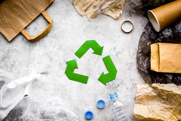 Eco-friendly life. Green paper recycling sign among waste paper, plastic, polyethylene on grey background top view