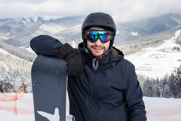 Portrait of cheerful snowboarder at top of ski slope at ski resort