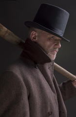 Portrait of a mature man dressed as a sinister Victorian criminal, with a wooden bat 