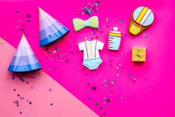 Celebrate child's birthday. Cookies in shape of baby accesssories, party hats, gift box, confetti on pink background top view