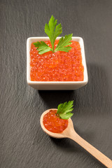 The wooden spoon with red caviar and parsley on black background. Close-up.