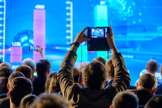 Man takes a picture of the presentation at the conference hall using smartphone