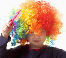 Humorous portrait of cute little girl brushing her colorful curly hair with comb. Hair beauty, hair care concept.