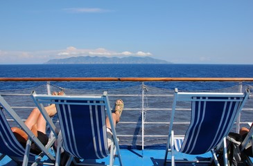 Obraz premium People relaxing on beach chairs on a ferry boat looking at Elba island, Tyhrrenian sea, Europe