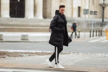 Foto auf Alu-Dibond Stylish man wolk on the street. Winter cold outfit. Big jacket with white sneakers. Blured background street. Profecional model photo. © Serhiy Hipskyy