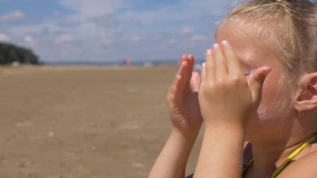 The girl apply sunscreen to face and body. The girl squeezes the sunscreen into her palm and puts it on her face.