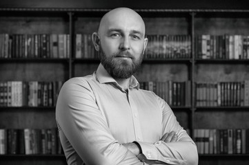 A bald man with a beard in the library.
Businessman.
Black and white photography.