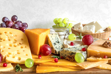 various types of cheese with grapes, rosemary and pomegranate on wooden cutting board