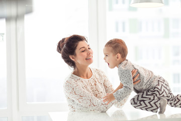 Beautiful woman and her cute little son are smiling and playing together at home. Young mother and kid together