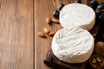 Camembert and brie cheese on wooden cutting board with grape and nuts.