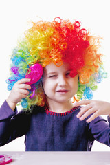 Humorous portrait of cute little girl brushing her colorful curly hair with comb. Hair beauty, hair care concept.