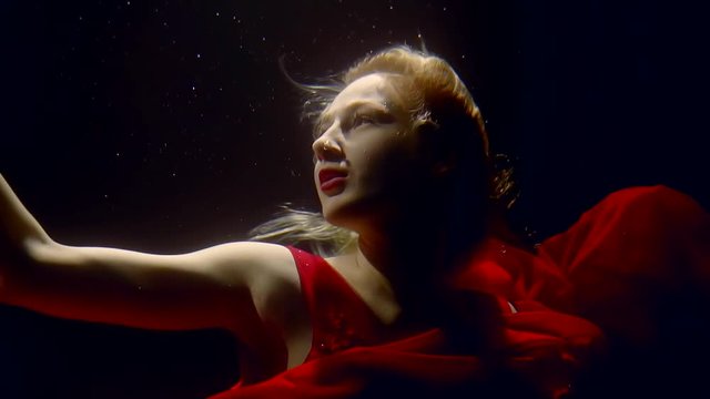 a woman in a red dress swims under the sea in the depths of the sea, she wants to duck before her reflection