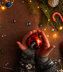 Girls hands holding Christmas ball. Dark table. Glowing light bulb. Festive accessories. New year. Christmas. The elements of design.