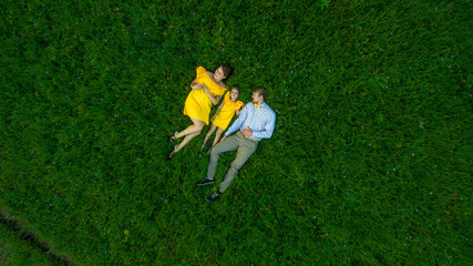 family lying on the grass. concept - father, mother and child daughter top view.. yellow clothes. summer sunny day. in green nature together. Drone view.