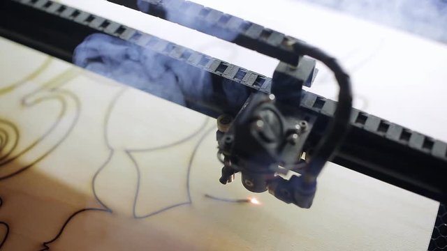 Machine for laser cutting wood close up cuts chipboard and the smoke appears.