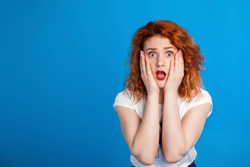 confused red-haired girl in the style of punk. Emotional concept. On brightly blue m background. Place for text.