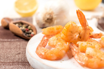 Grilled shrimps with lemon, paprika, spices and herbs on a white wooden board.