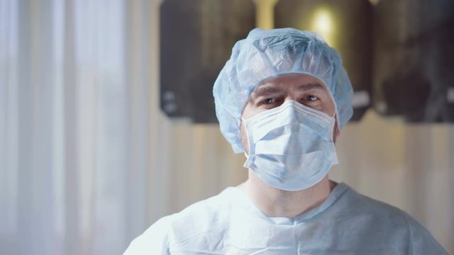 Young man doctor with mask looking at camera on x-ray background. Medical concept.
