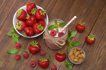 Pink strawberry and raspberry smoothie in a mason jar glass with straw and scattered berries