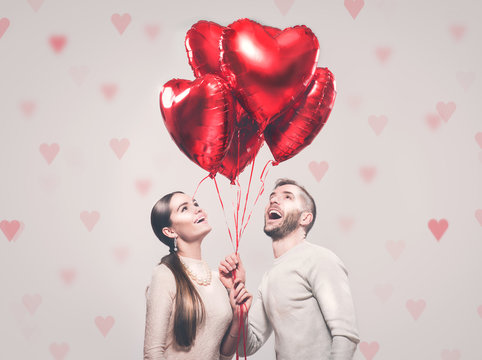 Valentine's Day. Happy joyful couple. Portrait of smiling beauty girl and her handsome boyfriend holding bunch of heart shaped air balloons