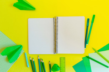 Fototapeta na wymiar Creative, fashionable, minimalistic, school or office workspace with green supplies on yellow background. Flat lay. Bank paper spiral notebook on yellow background.