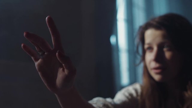 Insane like girl with shabby hair holds her hand, as trying to touch someone. No people around. Paranormal, moody atmosphere. Morning sun lighting the room