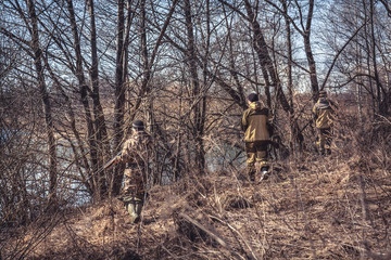 Obraz na płótnie Canvas Group of hunters in camouflage stealing in spring forest during hunting season