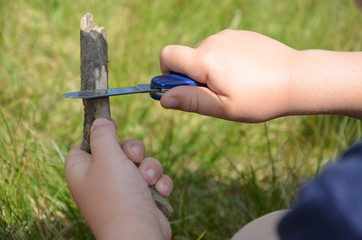Kind schnitzt mit einem Taschenmesser an einem Stück Holz