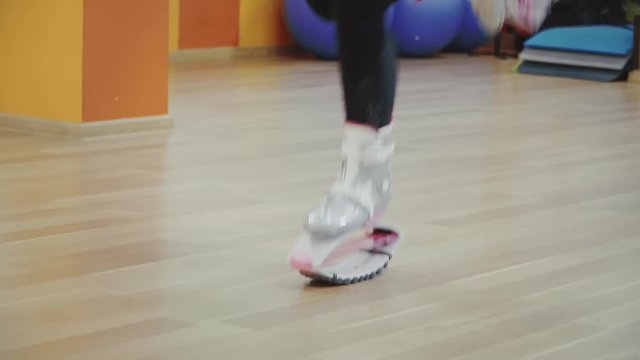 Blonde pretty young woman jumping in kangoo shoes in the gym.