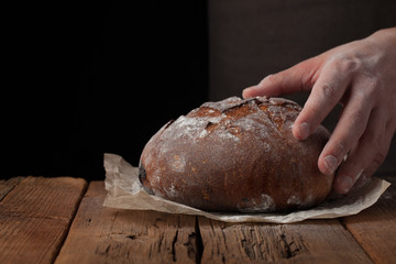Closeup of male hands put fresh bread on an old rustic table on black background with copy space for your text