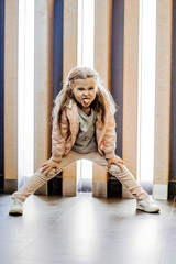 Little child in a pink suit poses near the wall