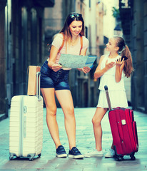 Mother and daughter travelers using paper map and phone