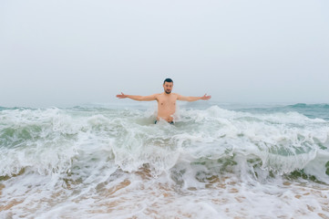Fototapeta premium Odd bizarre crazy fearless awesome adult man enjoying in cold stormy sea. Guy jumping in waves in ocean with emotional funny face. Adult male fooling like child in water outdoors. Leisure activities