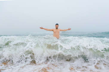 Odd bizarre crazy fearless awesome adult man enjoying in cold stormy sea. Guy jumping in waves in ocean with emotional funny face. Adult male fooling like child in water outdoors. Leisure activities