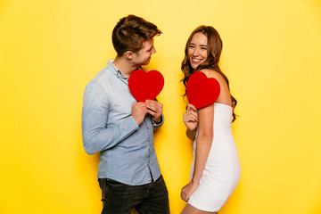 Attractive man and cheerful woman have fun together, holding red hearts during celebrating Valentine's day