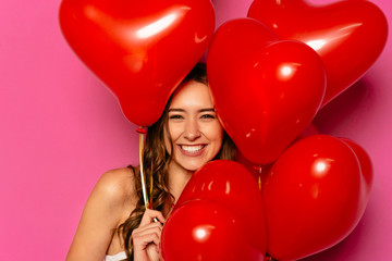 Happy Valentine's day. Gorgeous young woman, widely smiling, posing at camera with heart-shaped balloons.