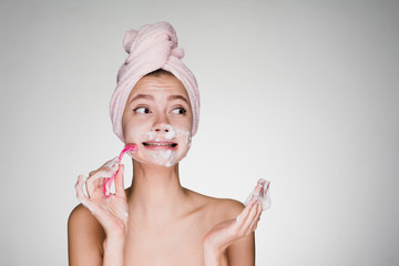 girl with a towel on her head performs facial hair removal with a razor - 188133525