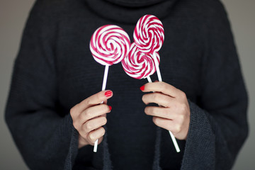 Woman hands with perfect nail polish holding some pink and white lollypops can be used as background