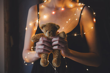 Female in black dress and lights holding teddy bear toy