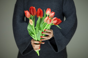 woman hands with perfect nail art holding red spring flowers tulips, sensual studio shot can be used as background