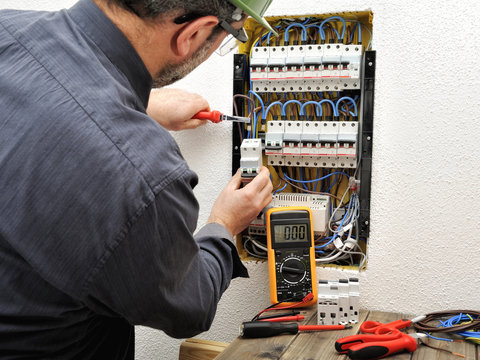 Electrician technician at work with protective helmet on a residential electric panel