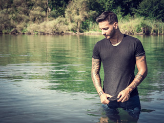 Young handsome tattooed man in wet clothes in the pond. 