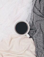 Cup of black coffee in white mug surrounded by different neutral toned fabrics. Flat lay. Top view. Copy space