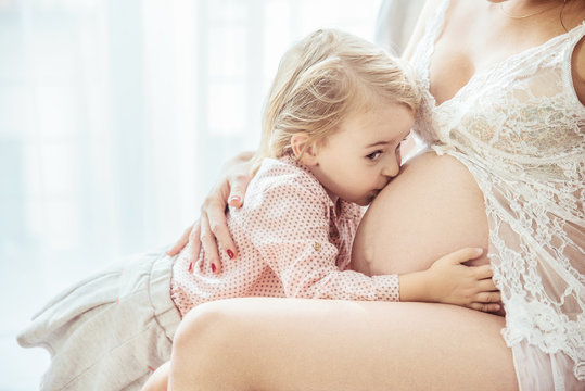 Cute little daughter kissing a mother's belly