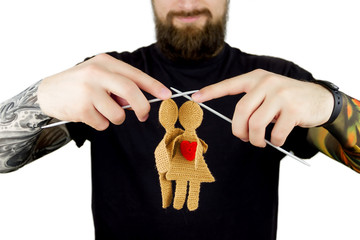 Strict man with tattoo and beard in black t-shirt holding knitted needles with knitted silhouette...