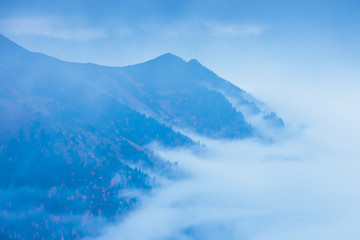 mountain landscape with fog below the peaks and clouds above them in blue tones