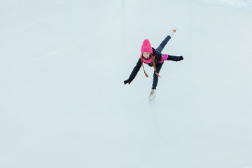 Little smiling girl skating on ice in pink wear. winter